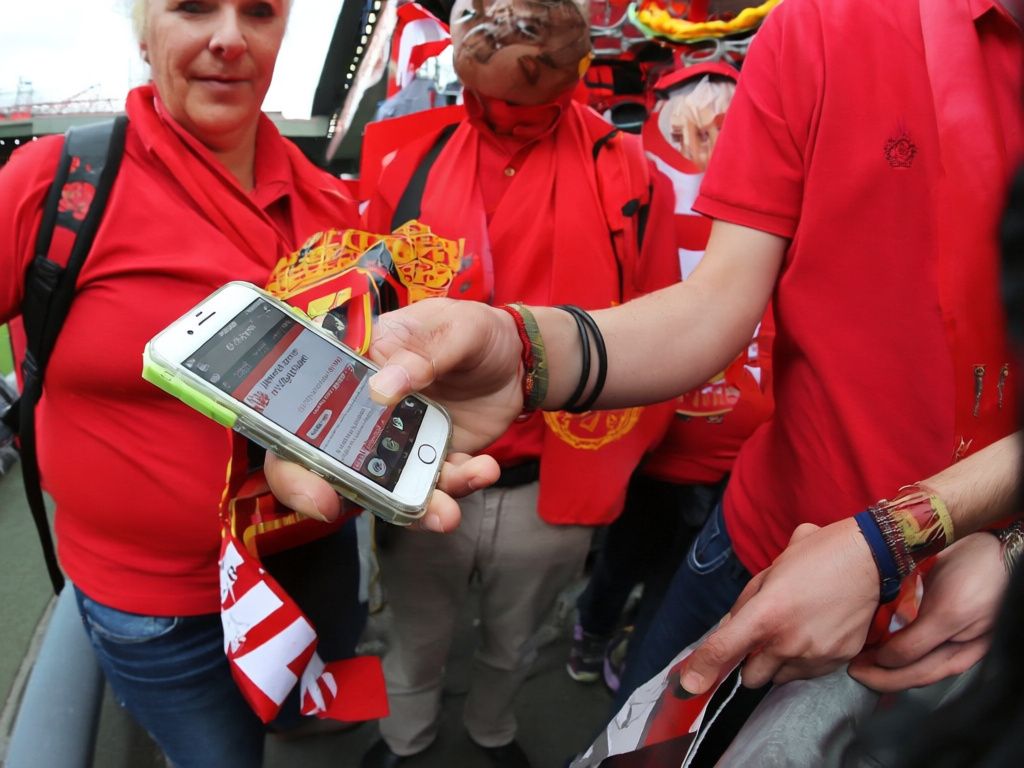 Manchester United supporters checking a fixture on a smartphone outside Old Trafford