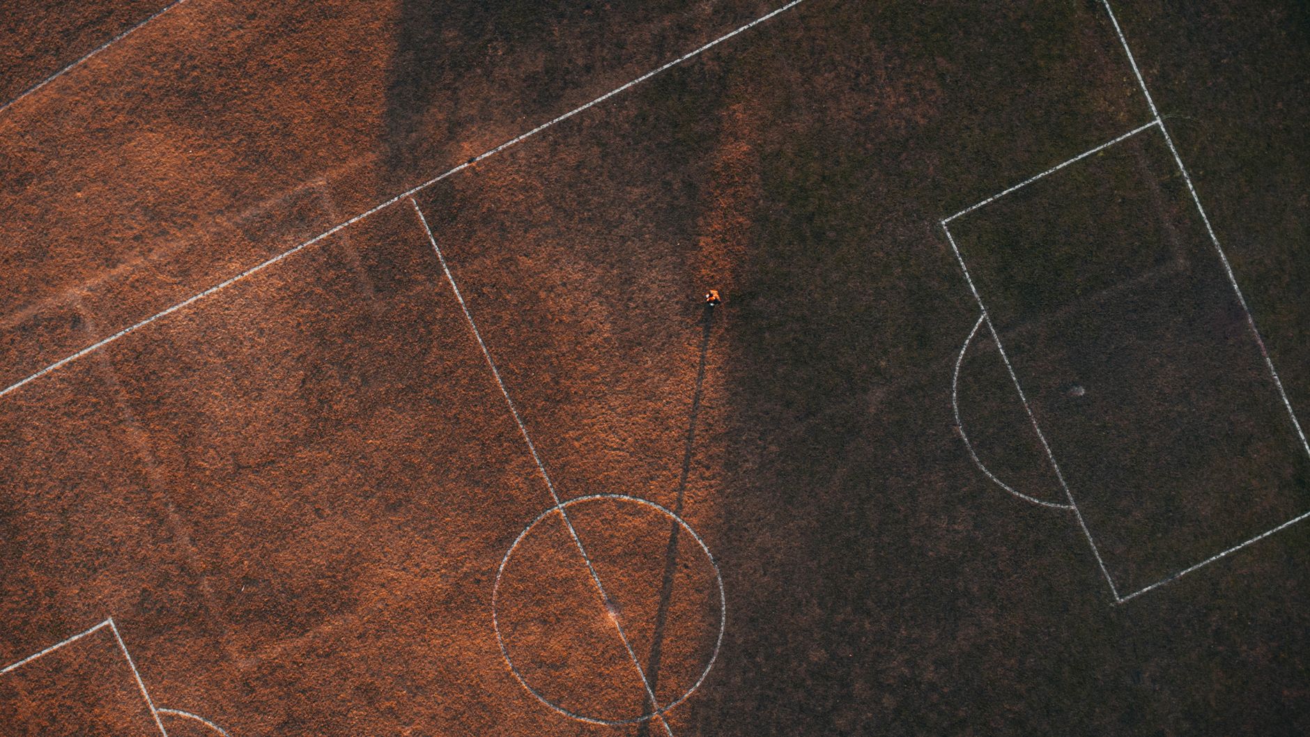 Aerial drone shot of a soccer field, highlighting markings and textures at dusk.