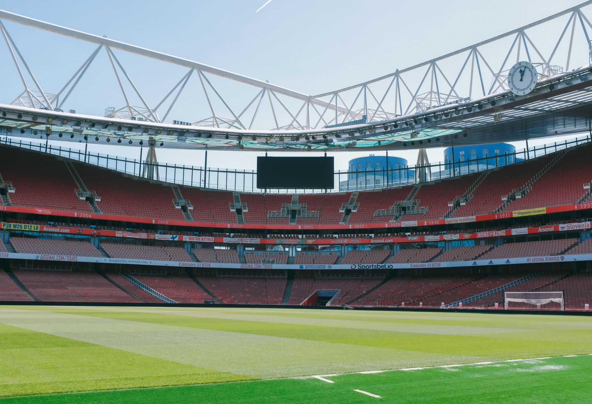 Empty soccer stadium with striking architecture in London, England, showcasing red seating and green pitch.